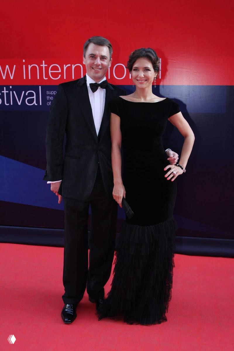 Игорь Петренко и женщина на красной дорожке в вечерних нарядах: пара улыбается и позирует для фотографов на фестивале.