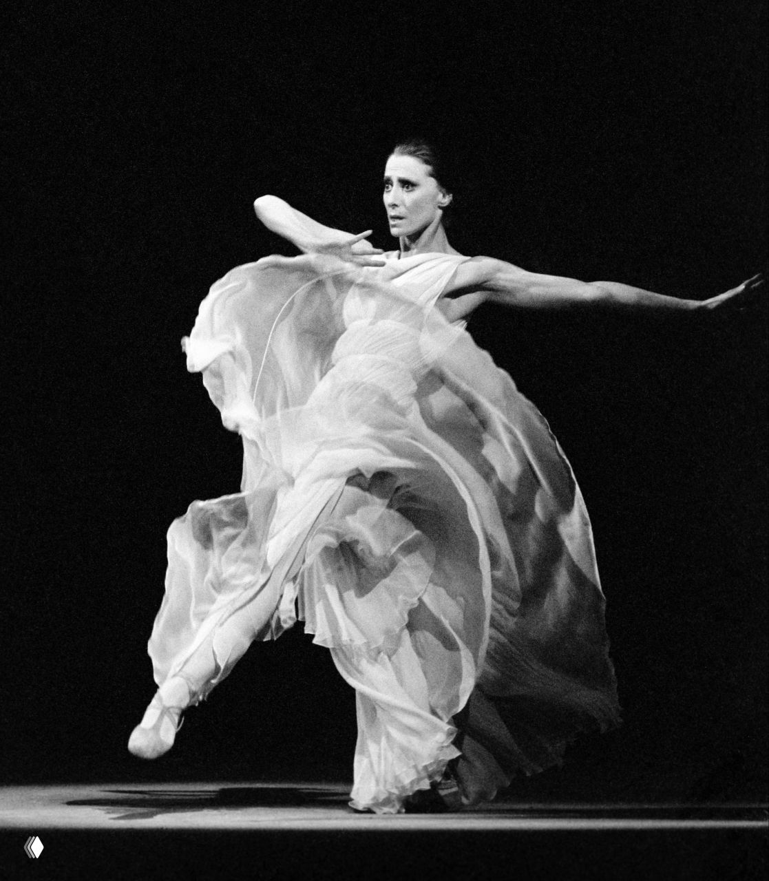 Чёрно‑белый динамичный кадр Майи Плисецкой в полёте во время спектакля: развевающийся костюм, выразительная поза и драматическая сцена классического балета