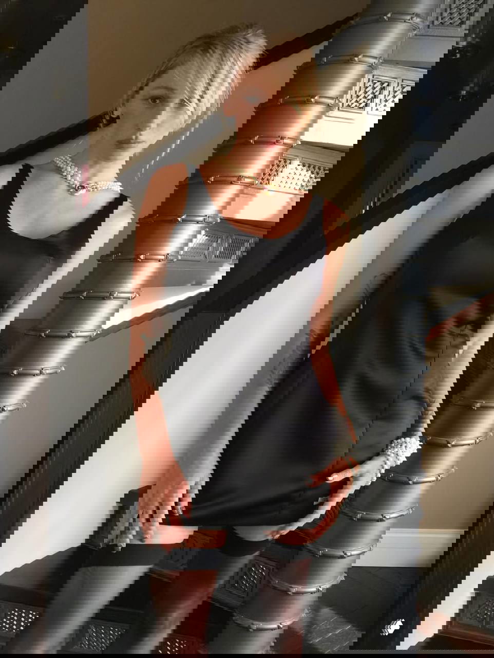 Полнотелый кадр: Настя Ивлеева в чёрном платье и на чулках позирует у лестницы, акцент на образе и украшениях.