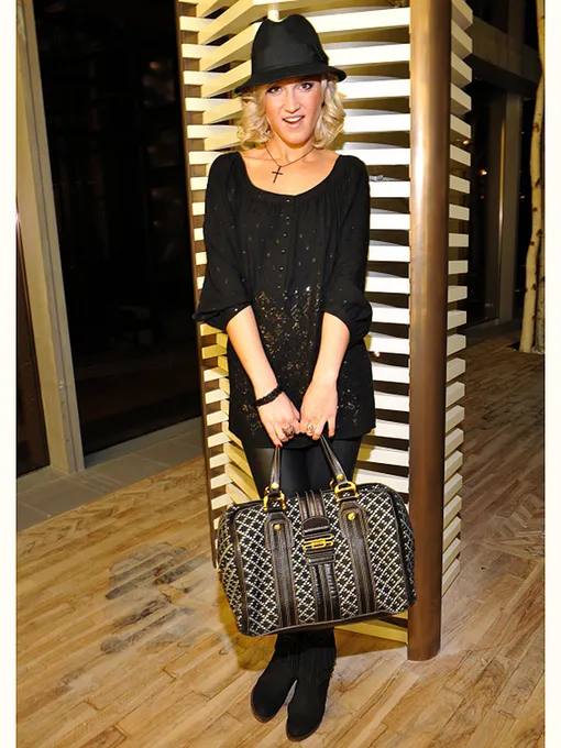 Женщина в чёрном свободном платье и шляпе с крупной сумкой на полу-фигурах, фото демонстрирует повседневный стиль в начале карьеры.