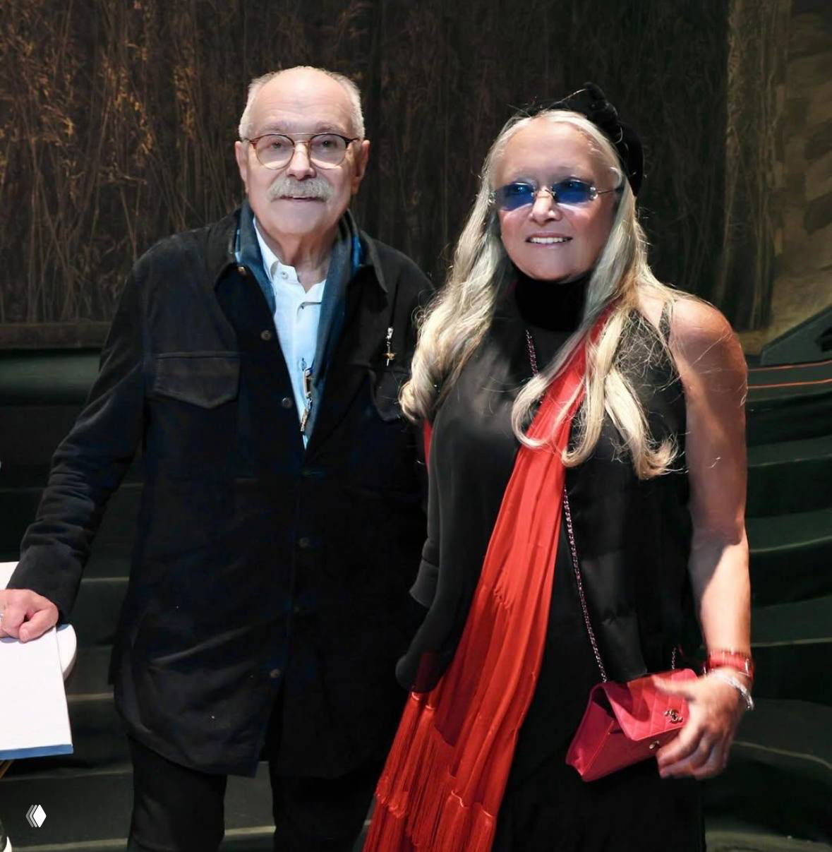 Портрет режиссёра в компании женщины в красном шарфе: неформальное фото гостей в интерьере зала.