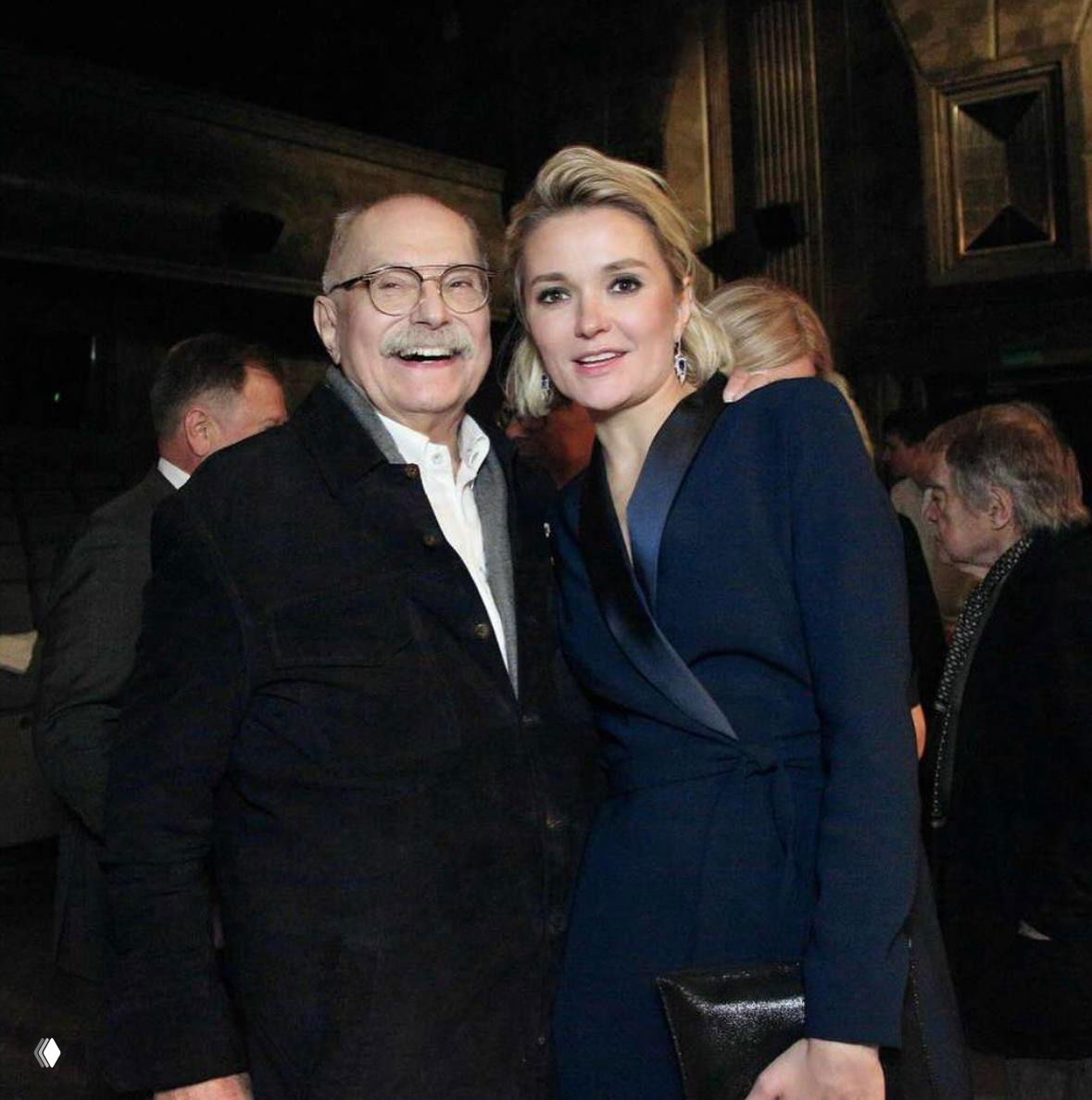 Режиссёр в тёплом общении с гостями на церемонии: тёплая поза, улыбки, камерная атмосфера юбилея.