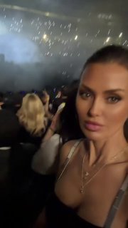 Кадр с концерта: крупный план селфи женщины на фоне затемнённой толпы и сцены, атмосфера вечернего шоу в Стамбуле.