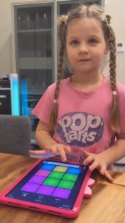 Маленькая девочка с косичками в розовой футболке играет на планшете с цветными блоками — кадр из домашнего видео.