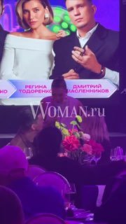 Крупный план экрана и композиции на столе с надписями и именами участников: на экране видны имена и графика премии, внизу цветы.
