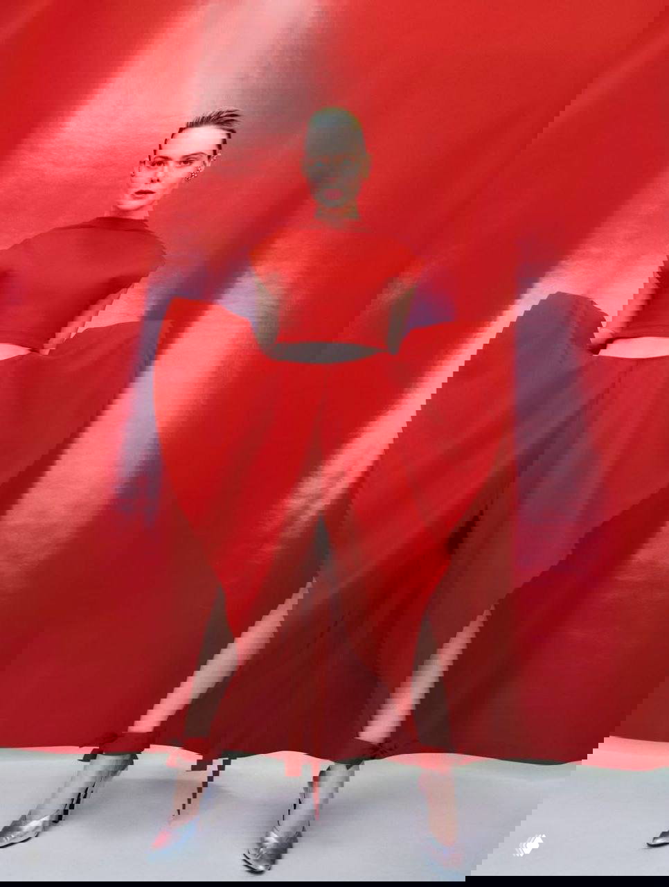 Эль Фаннинг в эффектном красном костюме на фоне глянцевой красной стены — полный рост, художественный модный кадр.