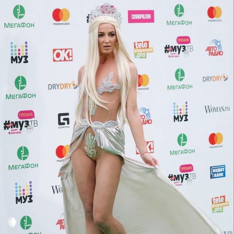 Женщина в эффектном сценическом костюме с обнажёнными элементами и пастельными волосами, фото с музыкального мероприятия или премии.