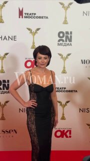 Екатерина Волкова в черном платье на красной дорожке церемонии «Ника», позирует на фоне бренд-стены и логотипов организаторов