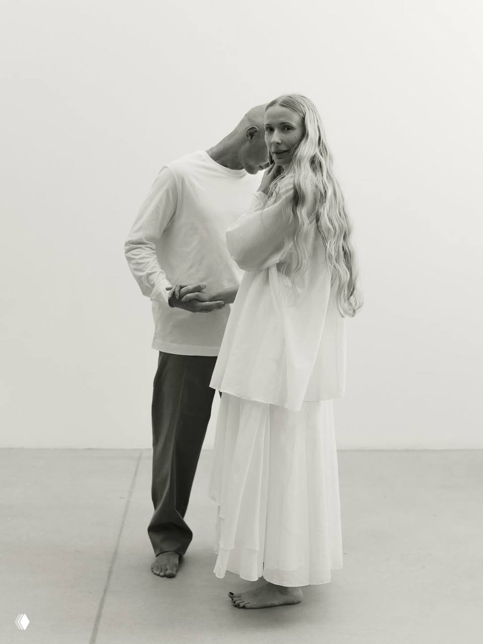 Портретная чёрно‑белая фотография пары в студии: женщина в длинном платье и мужчина стоят близко друг к другу в спокойной позе.