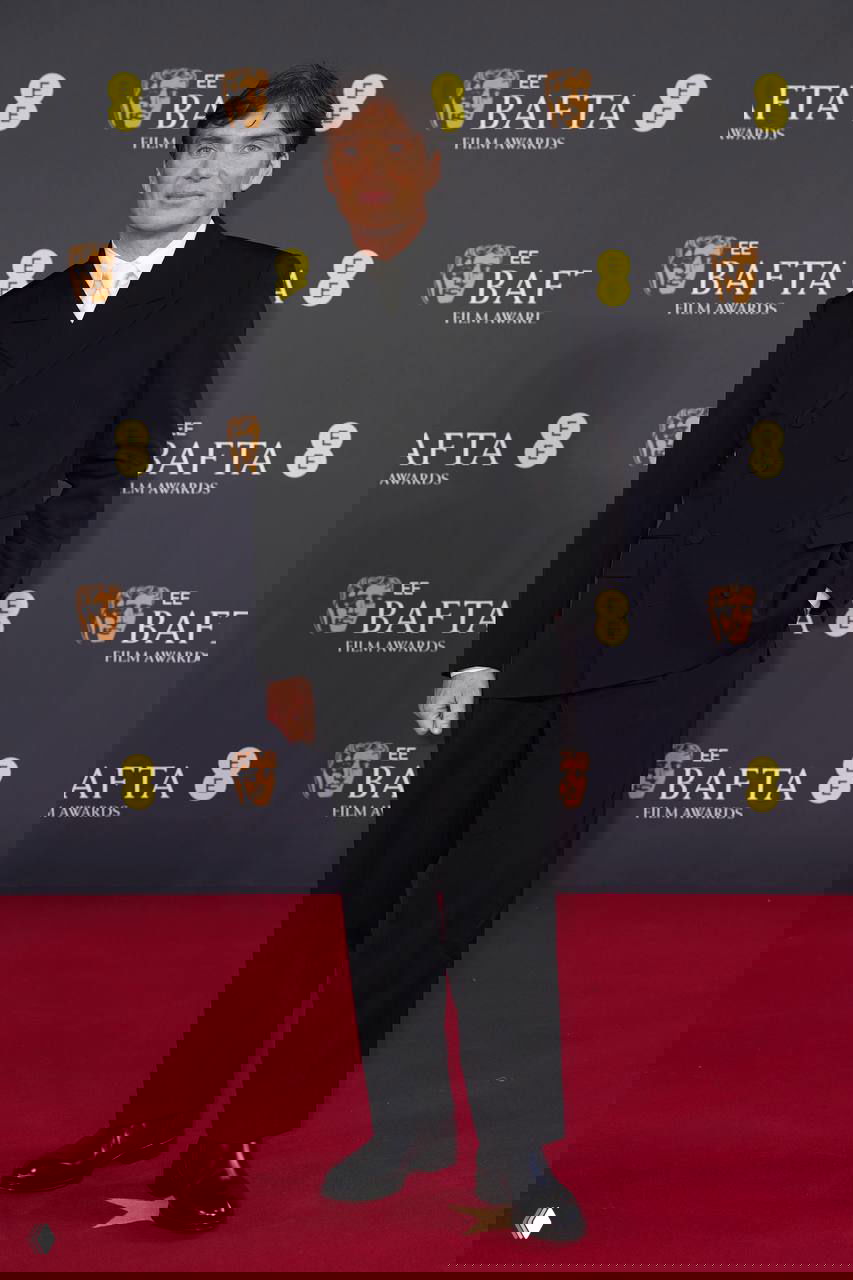 Киллиан Мёрфи в чёрном костюме позирует на красной дорожке BAFTA‑2026 на фоне фирменного баннера и логотипов.