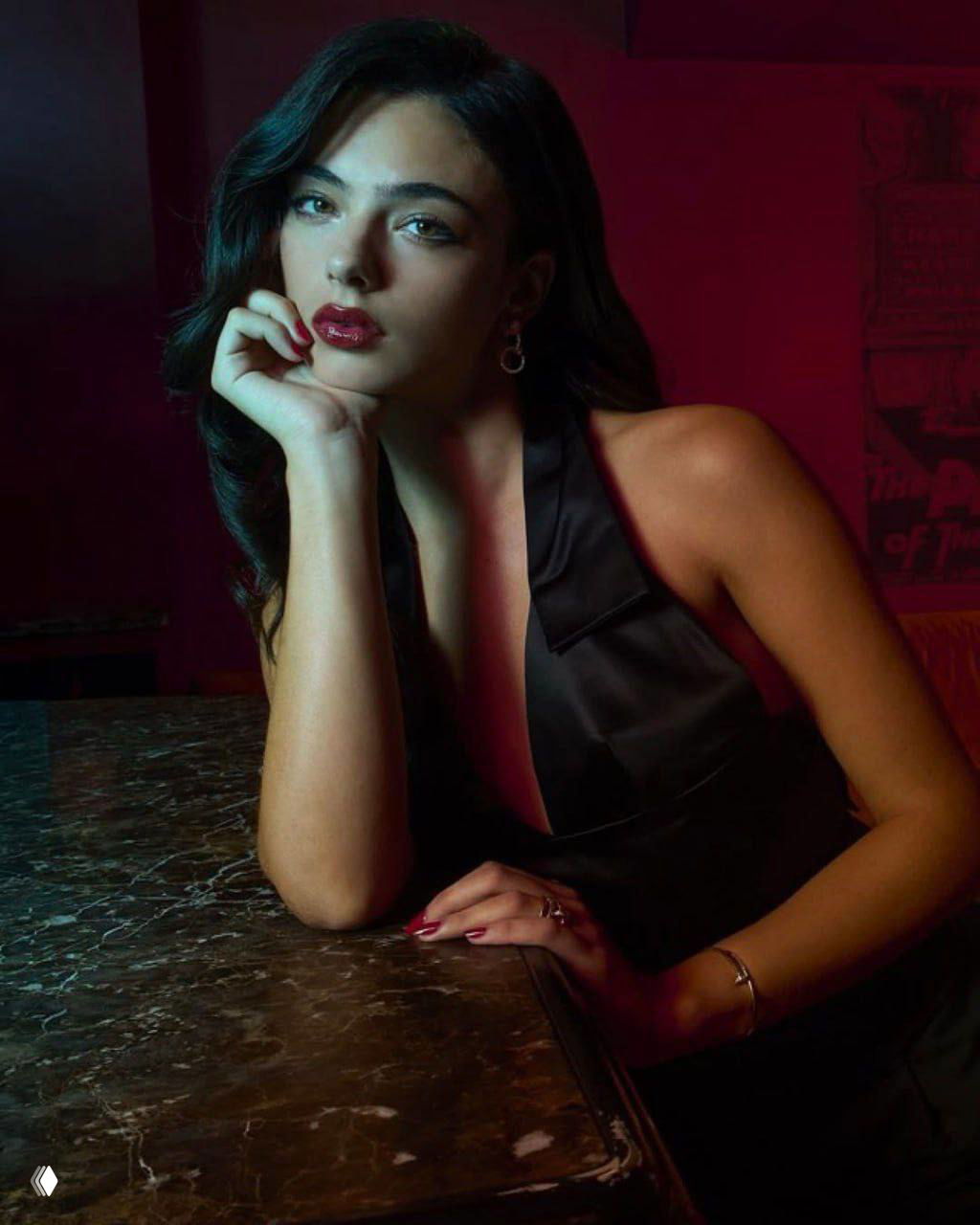 Портрет женщины в гламурном образе: тёмные волосы, насыщенная красная помада, поза у стола в интерьерной фотосессии.