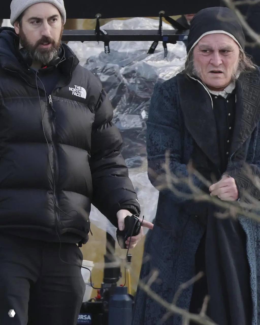 Сцена с оператором и актёром в старинном костюме: на заднем плане видна кинематографическая аппаратура и часть съёмочной команды на улице.