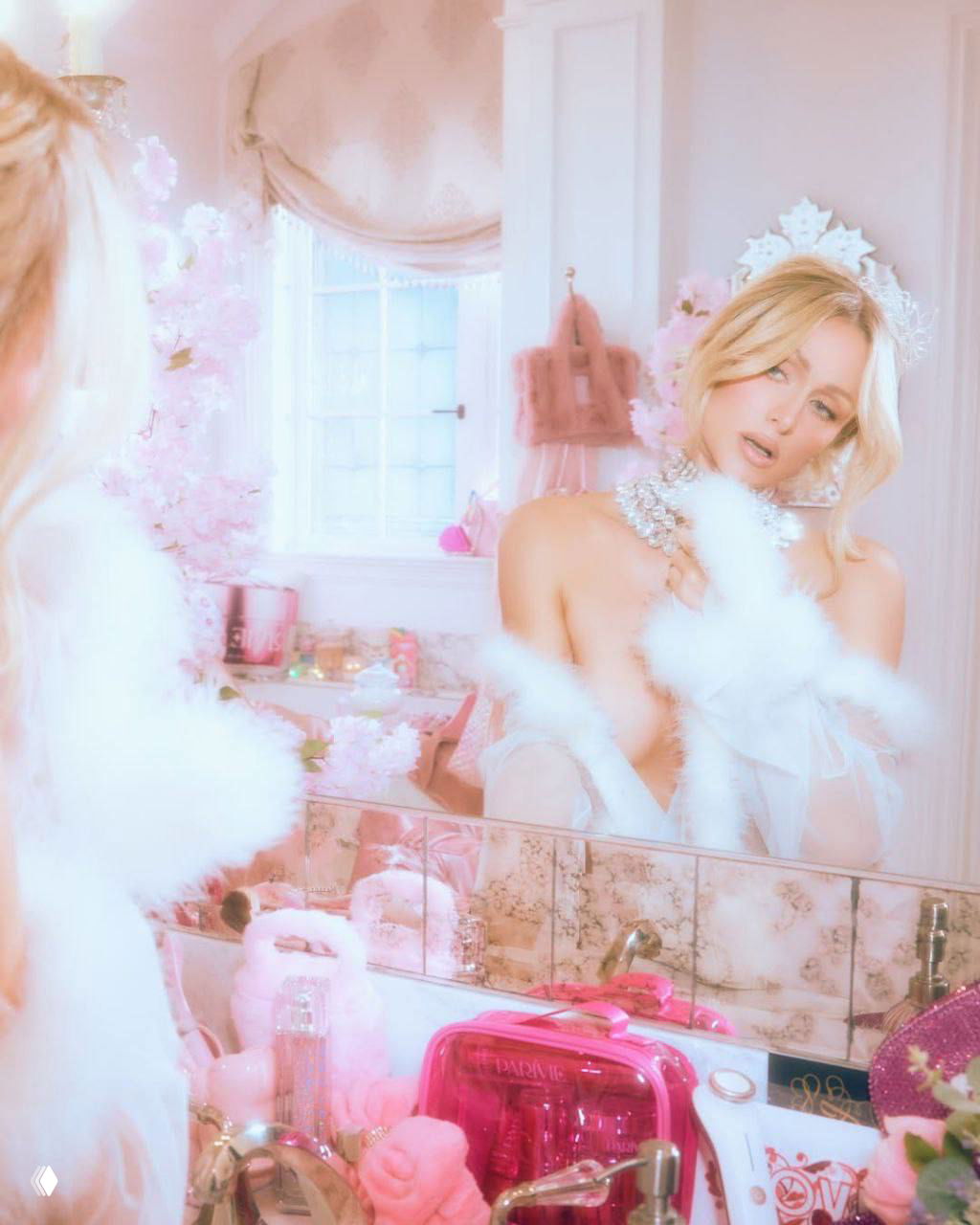 Отражение Пэрис Хилтон в зеркале косметической комнаты: розовый интерьер, полупрозрачный наряд и косметические аксессуары на переднем плане.