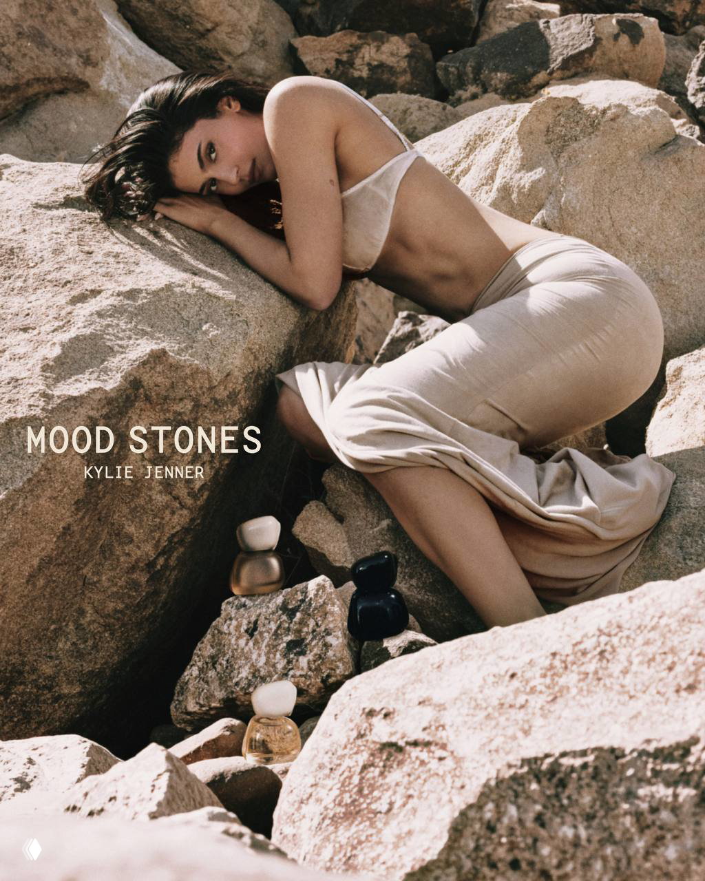 Кайли Дженнер позирует на скалах рядом с флаконами парфюма Mood Stones; натуральная палитра и текстуры камней в съёмке.