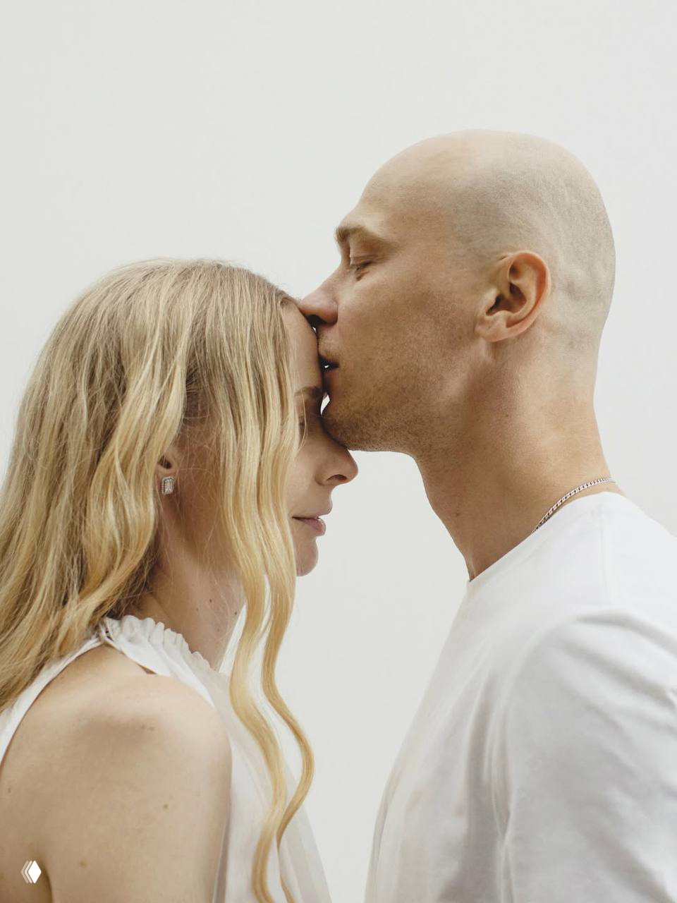 Интимный кадр пары в студии: мужчина стоит за женщиной и нежно обнимает её, тёплые цвета и кинематографичная постановка.