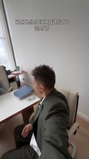 Кадр из видео: молодой мужчина в пиджаке сидит за столом в помещении ЗАГСа, вид со спины; на видео текст «КАК МЫ СХОДИЛИ В ЗАГС».