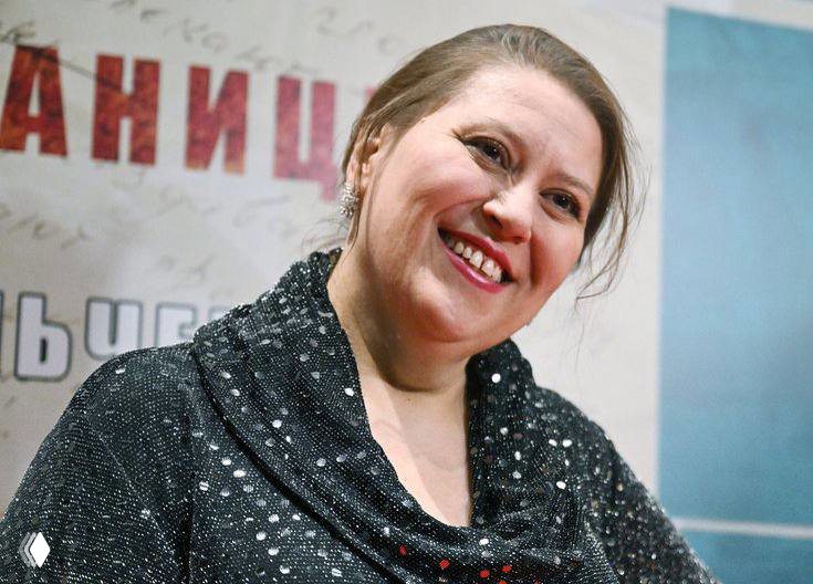 Татьяна Плетнёва улыбается на фотоколле: средний план, актриса в тёплой одежде на фоне баннера, дружелюбный портрет.