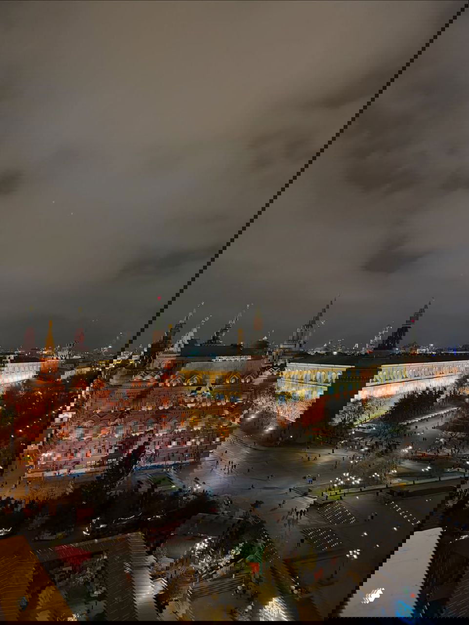 Ночной вид на Красную площадь и Кремль в Москве с подсветкой исторических зданий и редкими прохожими на площади.