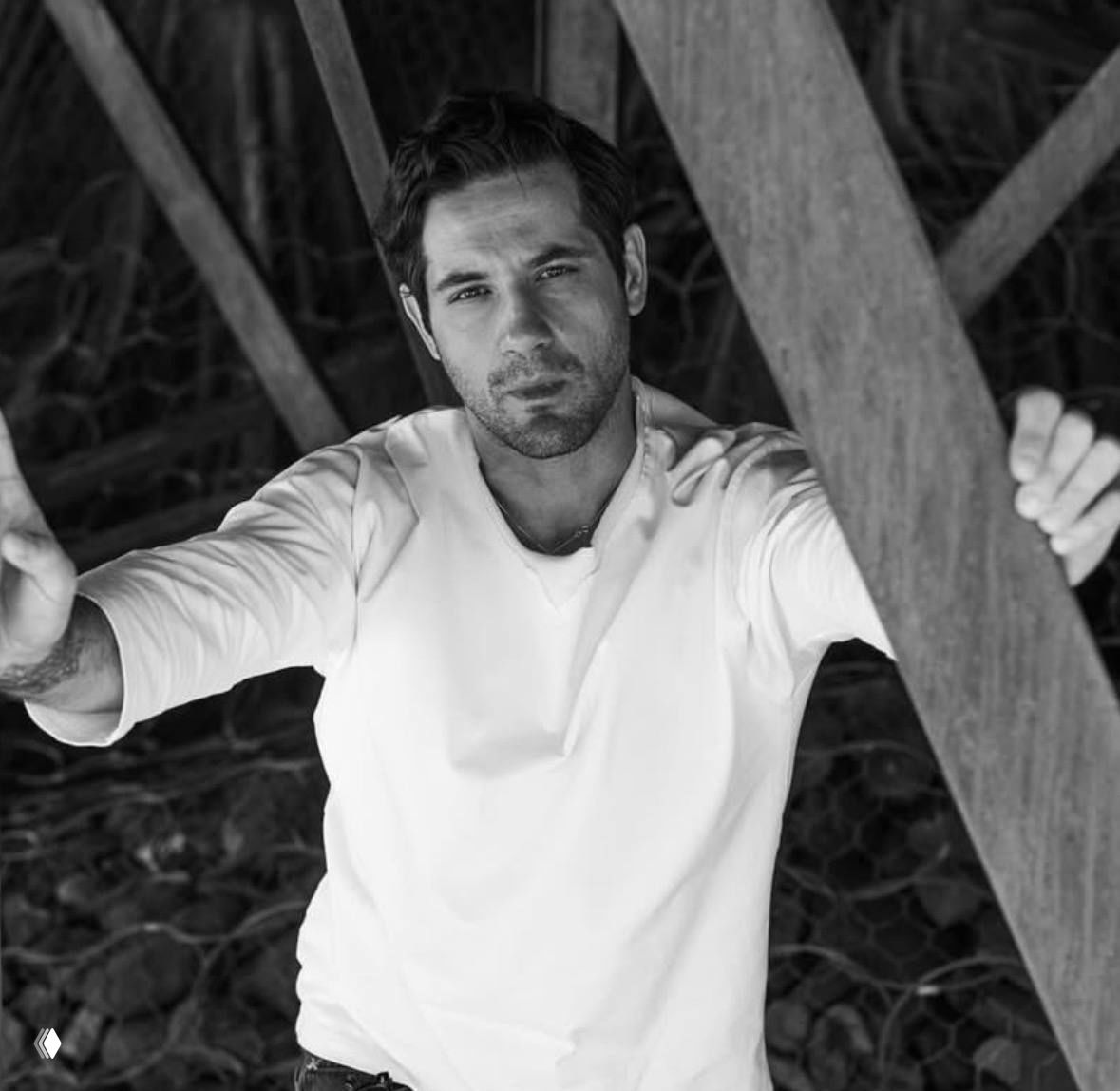 Портрет в чёрно‑белых тонах: мужчина смотрит в камеру, руки обрамляют кадр; интерьерный художественный снимок крупным планом.