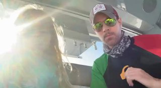 Два человека на лодке: взрослый в кепке и солнцезащитных очках и маленькая девочка рядом, яркое солнце создаёт контровый свет и блики на кадре.