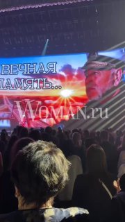 Зал с публикой и сцена: на большом экране надпись «Вечная память...» и фото пожилого мужчины — кадр с выступления.
