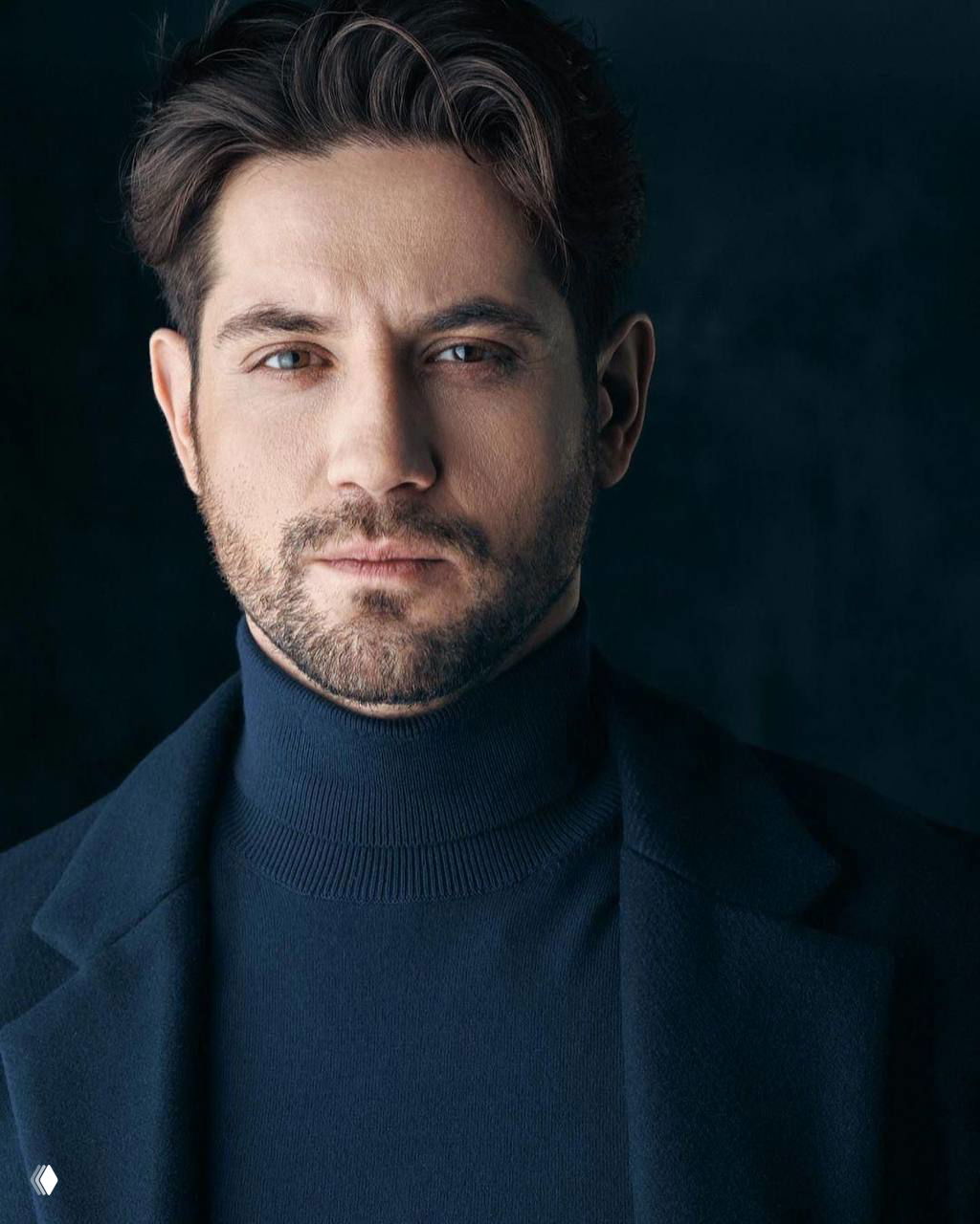 Крупный студийный портрет мужчины в тёмном водолазке и пиджаке; деликатное освещение подчёркивает черты лица, профессиональная съёмка.