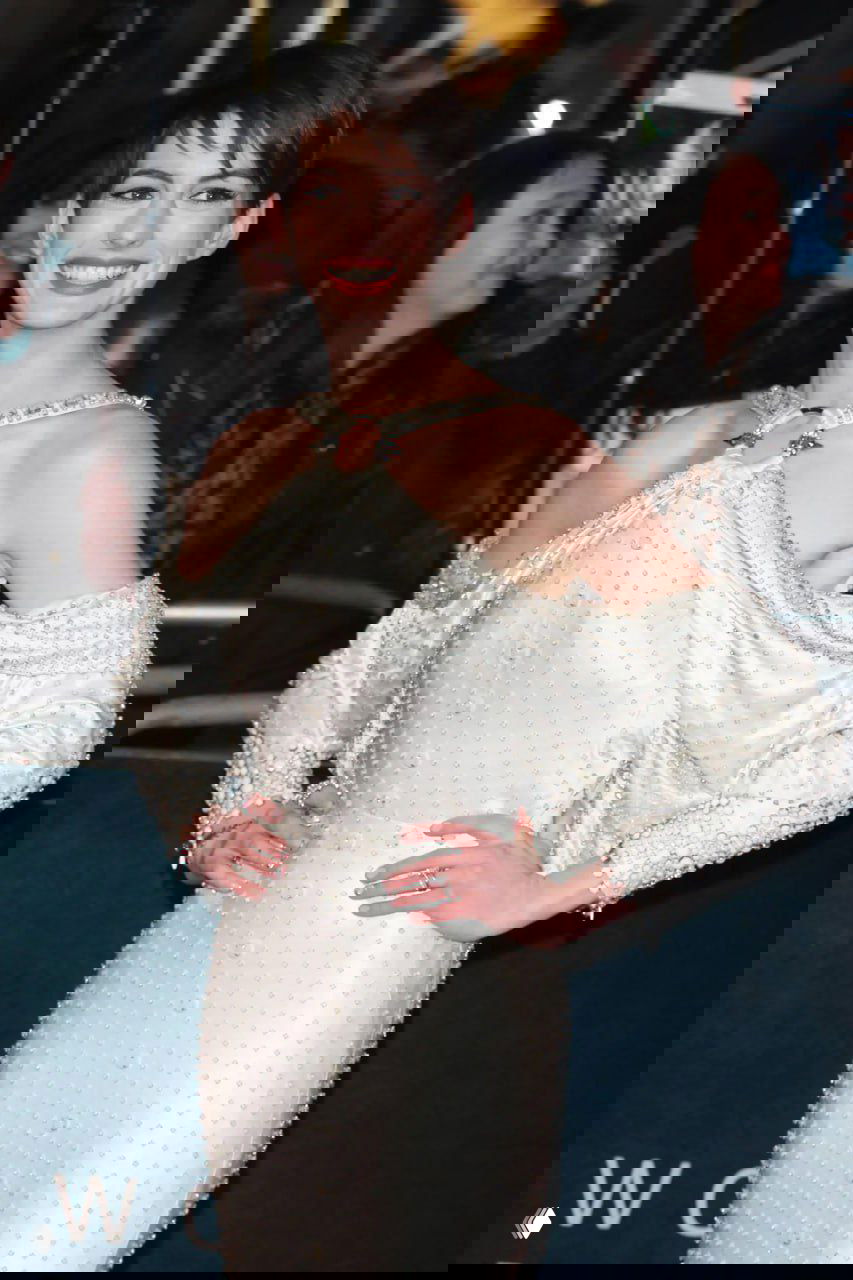 Энн Хэтэуэй в светлом наряде с открытыми плечами и короткой стрижкой; образ в стилистике красной дорожки с акцентом на украшения.