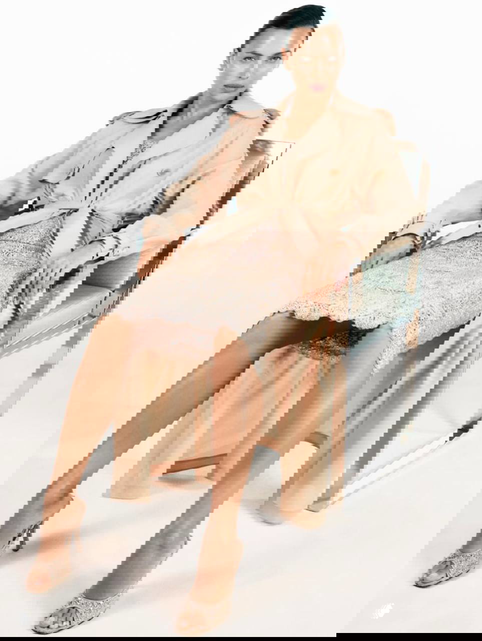 Ирина Шейк в светлом тренче и кружевном платье из кампейна Ermanno Scervino; сидит в кресле, образ в пастельных тонах и тонкой фактуре.