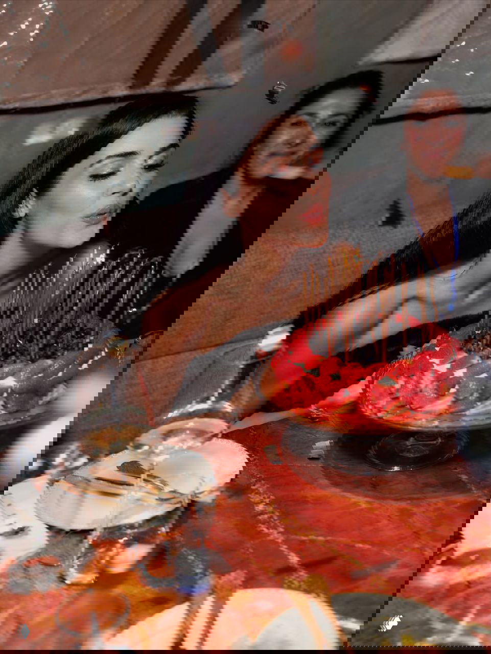 Крупный план: Ханде Эрчел задувает свечи на клубничном торте во время празднования дня рождения, свечи и торт в центре кадра.