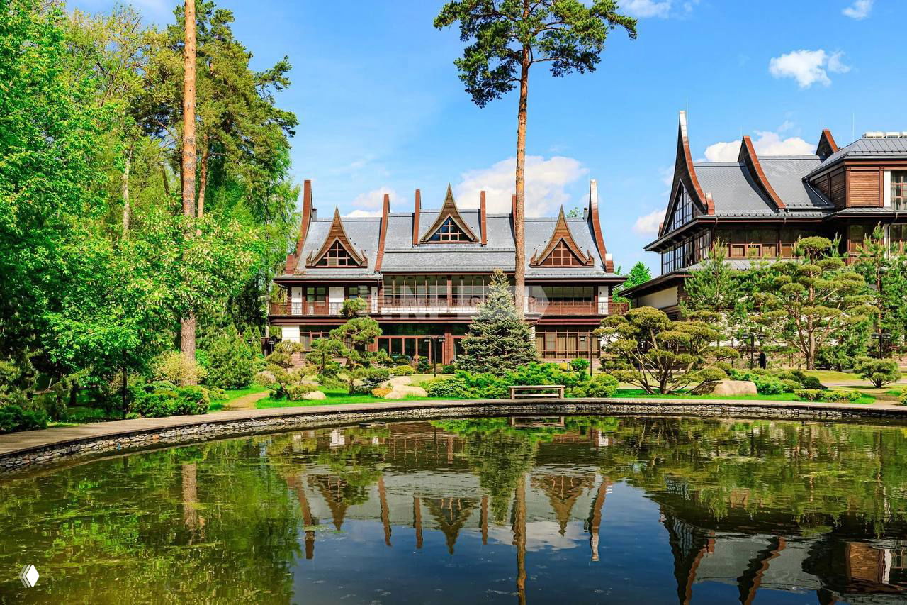 Внешний вид большой резиденции в тайском стиле на участке с ухоженным садом и декоративным прудом: фасад особняка отражается в воде.