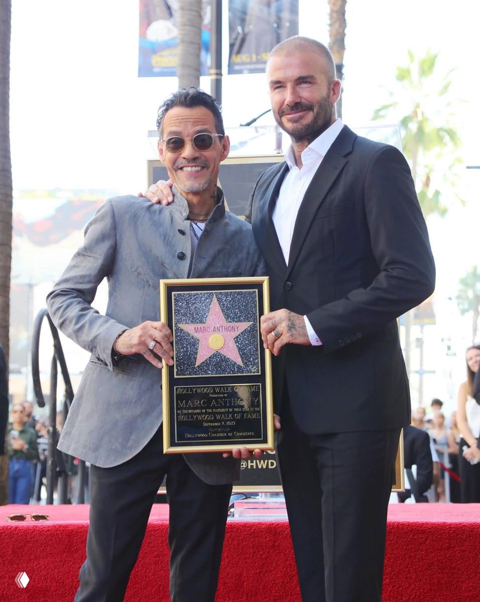 Двое мужчин на уличной церемонии держат рамку с табличкой «звезда»: один в очках улыбается, на заднем плане видны пальмы и прохожие.