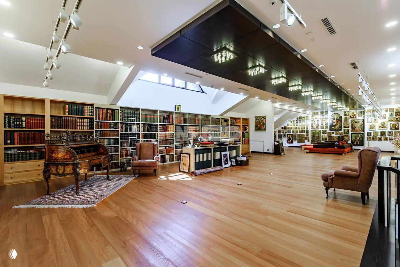 Просторный зал с библиотекой и множеством картин на стенах, большими полками и зонами для работы — возможный продюсерский центр внутри резиденции.