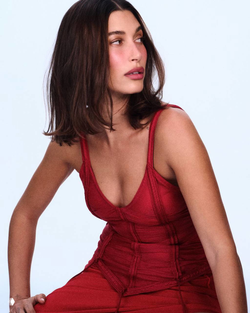 Цветная фотография Хейли Бибер в красном платье из фотосессии Rhode: сидящая поза, мягкий свет, акцент на силуэт, текстуру ткани и минимальную ретушь.