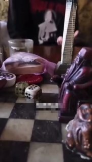 Кадр из видео: шахматная доска с фигурками и игровыми кубиками, на столе предметы и фрагмент руки, размыт фон интерьера