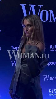 Женщина в серебристом наряде на фоне фиолетового баннера Woman.ru; фото сделано на вечеринке Celebrity Party в Kiki Event Dom.