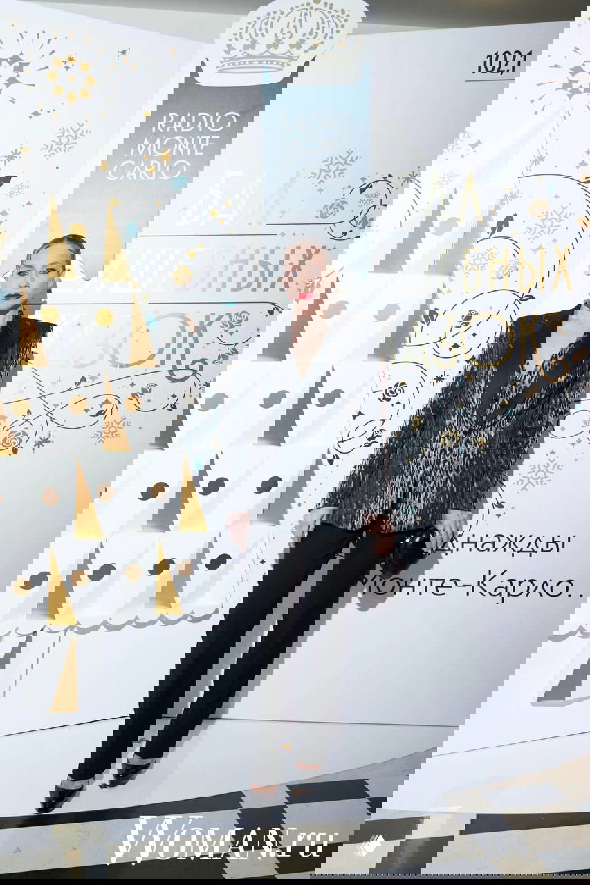 Женщина в строгом вечернем костюме позирует у брендволла Radio Monte Carlo на светском мероприятии «Бал волшебных сказок».