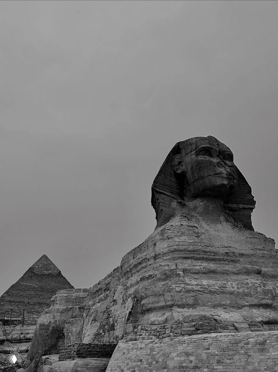 Чёрно‑белый кадр Большого Сфинкса и пирамида на заднем плане: крупный план головы сфинкса и текстуры древнего камня.