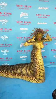 Хайди Клум позирует в образе Медузы Горгоны на синей фотозоне: вид в полный рост с акцентом на хвост и текстуру костюма.