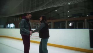 Два человека на льду во время репетиции шоу: мужчина и женщина стоят у борта катка, держатся за руки и общаются в спортивной обстановке.