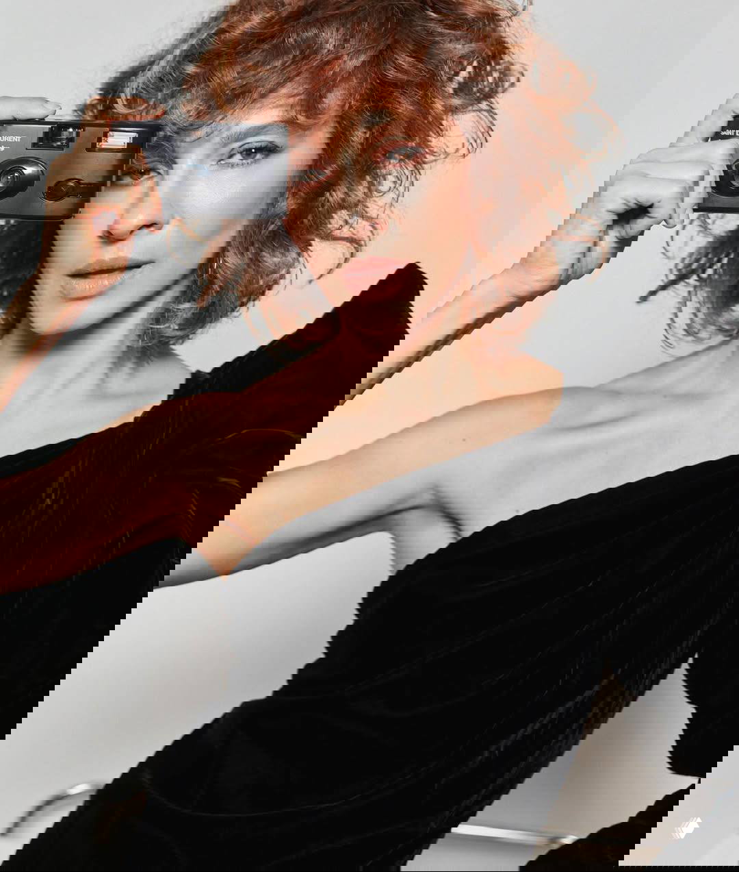 Крупный план Елены Подкаминской с компактной камерой в руке: чёрное платье на одно плечо, естественный макияж и спокойный взгляд.