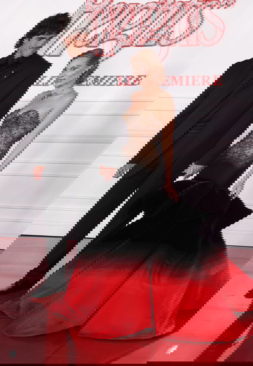 Актриса и спутник на фотозоне: платье Schiaparelli с чёрным кружевным корсетом и ярко‑красным пышным низом, кадр с премьеры в Лос‑Анджелесе.