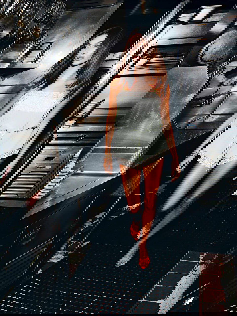 Фотография в интерьерной локации — модель в коротком комбинезоне идёт по проходу профессиональной кухни, fashion‑стилизация