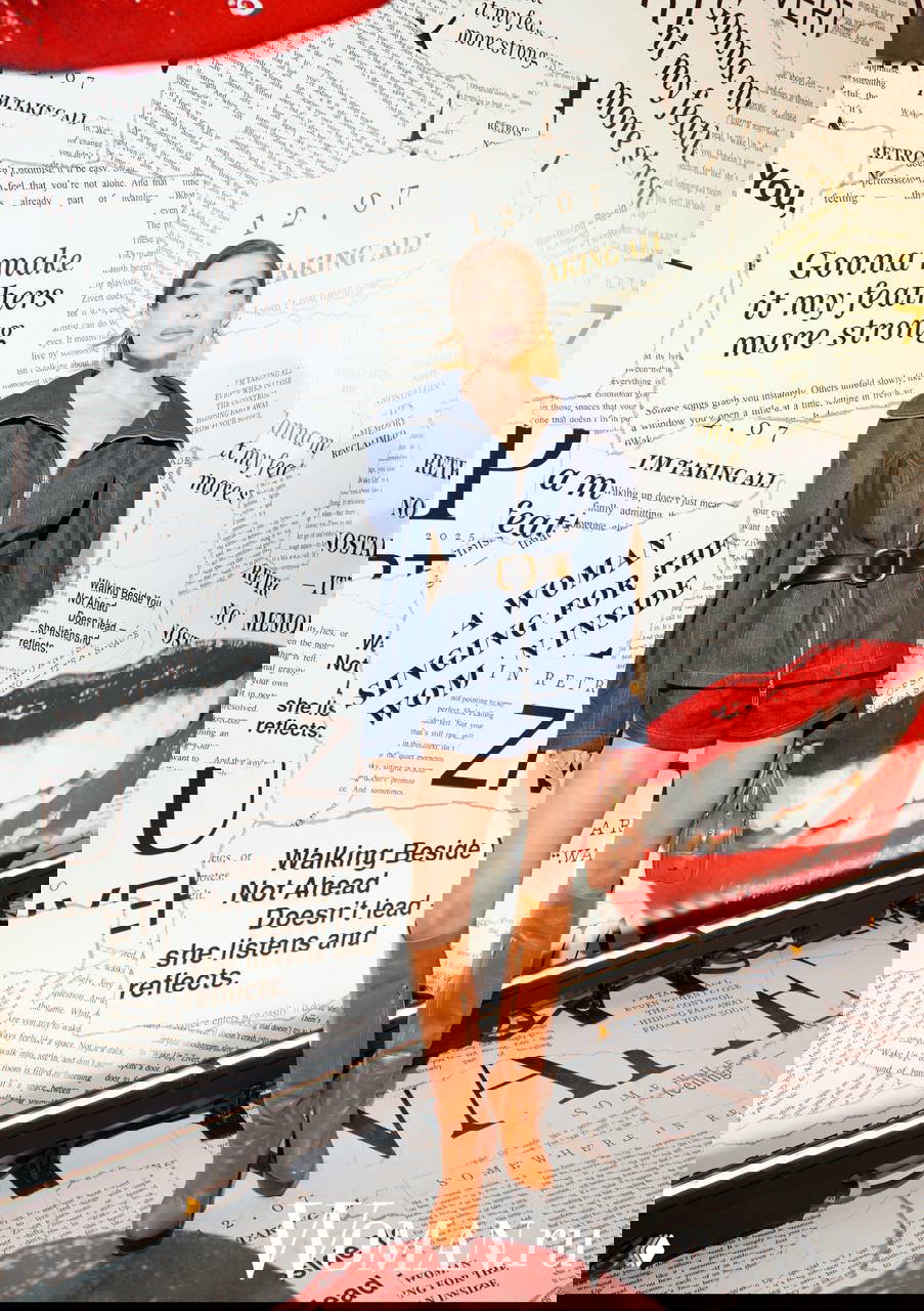 Молодая женщина в джинсовом костюме и высоких сапогах позирует перед тематической стеной с газетным принтом и крупными губами из оформления шоу