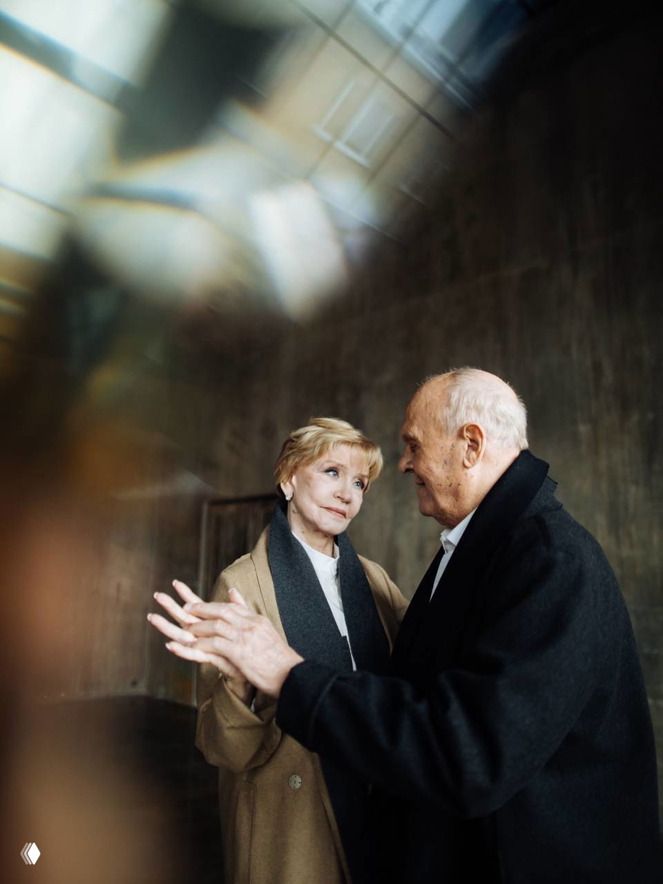 Широкий кадр пожилой пары в интерьере с мягким рассеянным светом; композиция подчёркивает эмоции, память и торжество чувств.