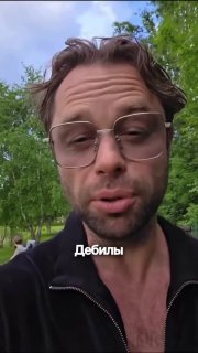 Крупный план Виталия Гогунского в очках на улице с текстом «Дебилы» — кадр из его видеообращения, обращённого к подписчикам.