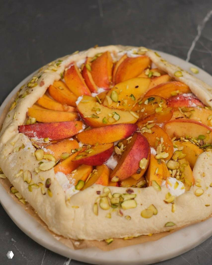 Фруктовый галет с дольками персика и посыпкой из дроблёных фисташек на тарелке — домашняя выпечка как часть заготовок и десертов.