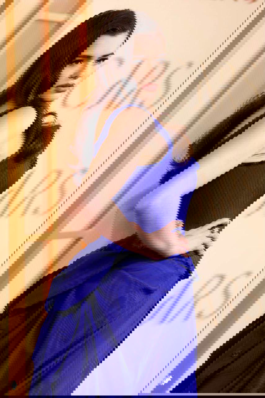 Крупный план Барби Феррейры в корсетном верхе синего платья на фоне бэкдропа с надписью OSCARS: профиль, причёска и детали кроя наряда.