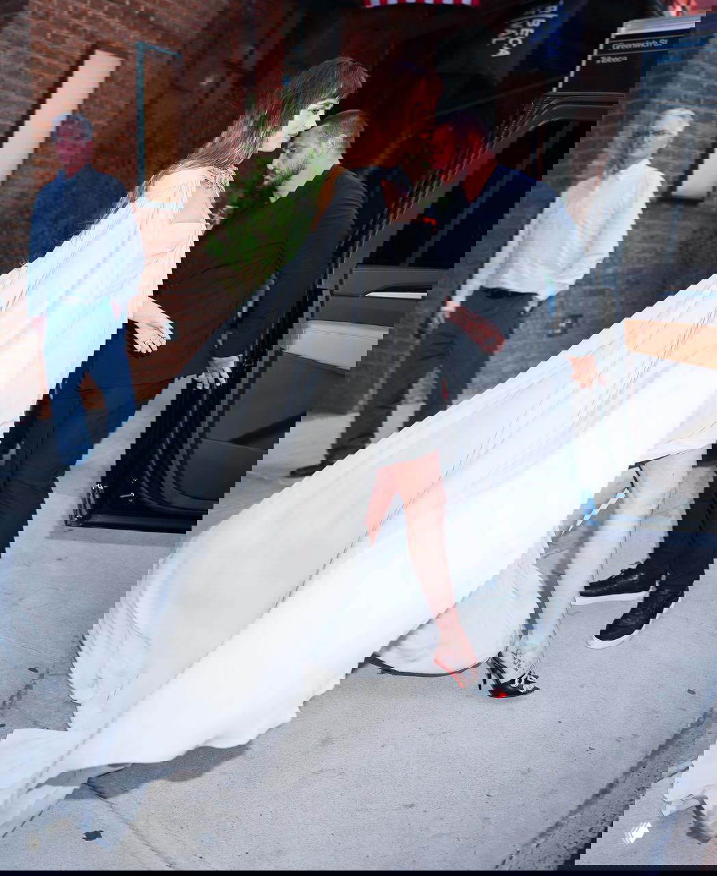 Дакота Джонсон выходит из машины в длинном белом плаще на красной дорожке, кадр в профиль с развевающейся накидкой и движением ткани.