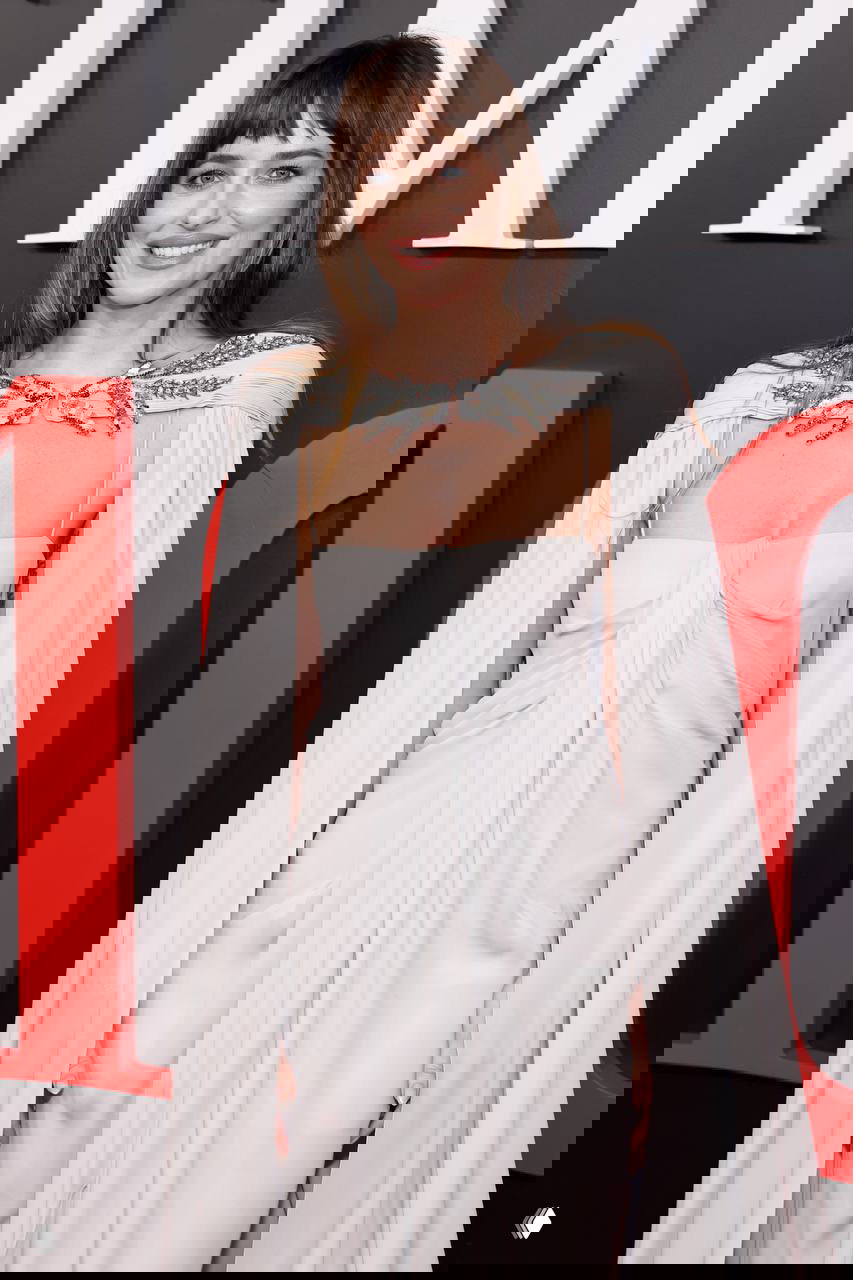 Крупный план Дакоты Джонсон в белоснежном платье с украшением на плечах на фоне логотипа TIME, улыбается в камеру.