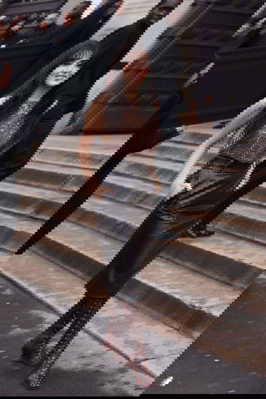 Фото на лестнице при показе Elie Saab: Ханде Эрчел идёт по ступеням в кожаной юбке и высоких коричневых ботинках, вокруг видна уличная атмосфера и люди шоу.